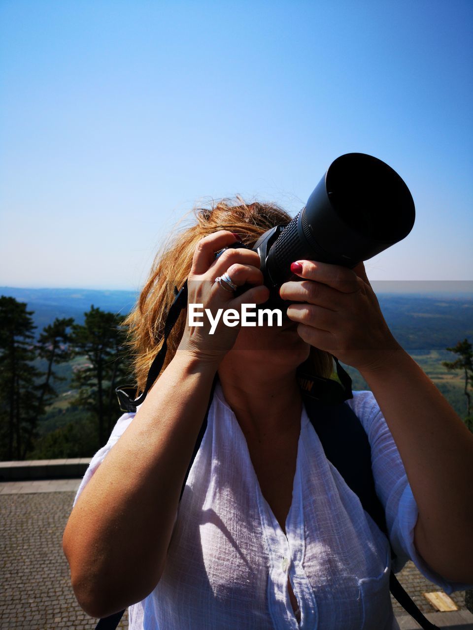 Woman photographing while standing on mountain against clear sky