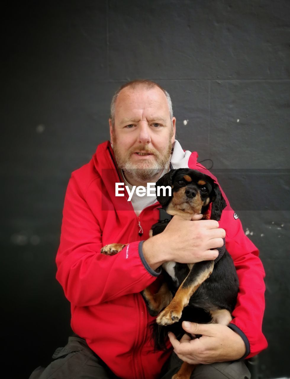 Portrait of mature man holding dog while sitting against wall