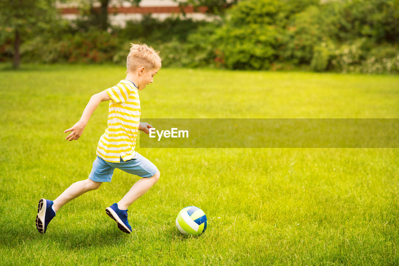 Full length of boy playing with ball on grass