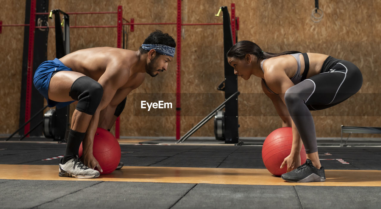 Concentrated sportswoman and sportsman doing squats with heavy medical balls during functional intense training in sports club