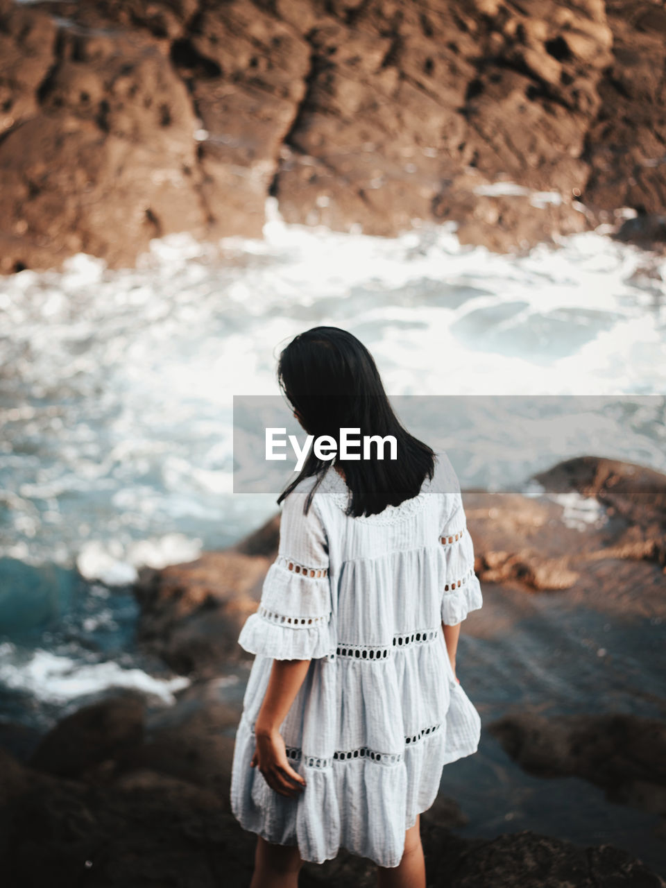 Rear view of woman standing on rock by sea