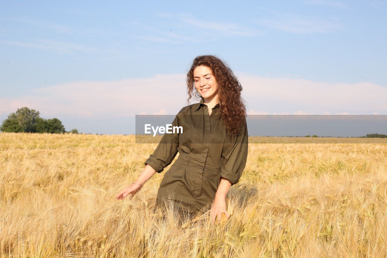 Happy woman standing on field against sky