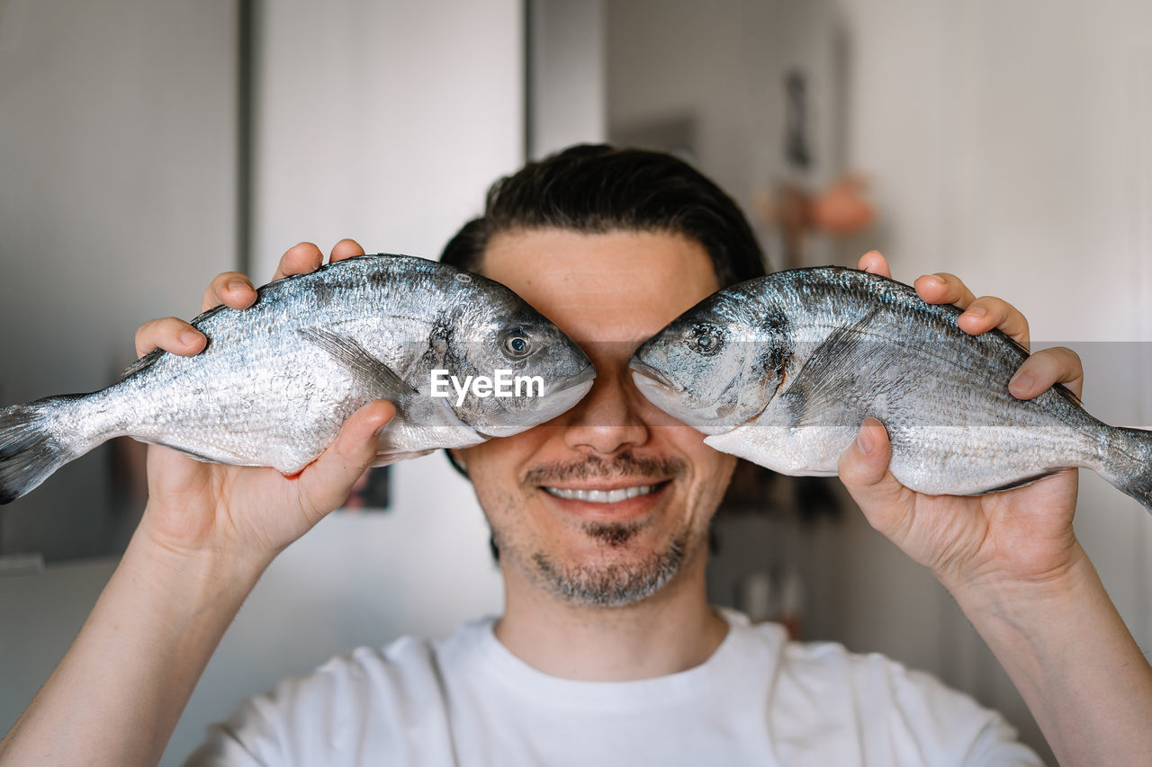 Funny portrait of man holding fish in kitchen