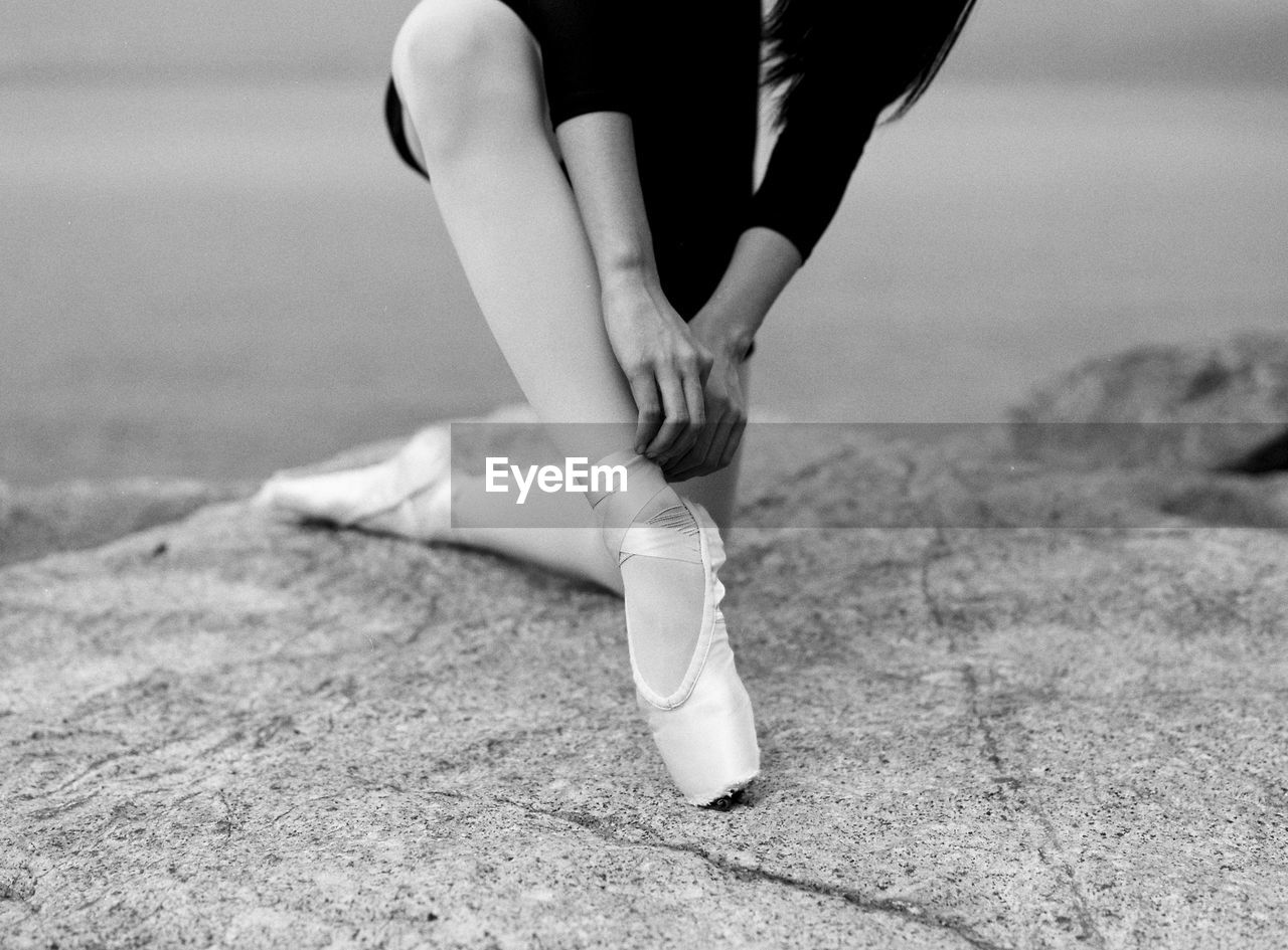 Midsection of ballerina tying shoe on rock