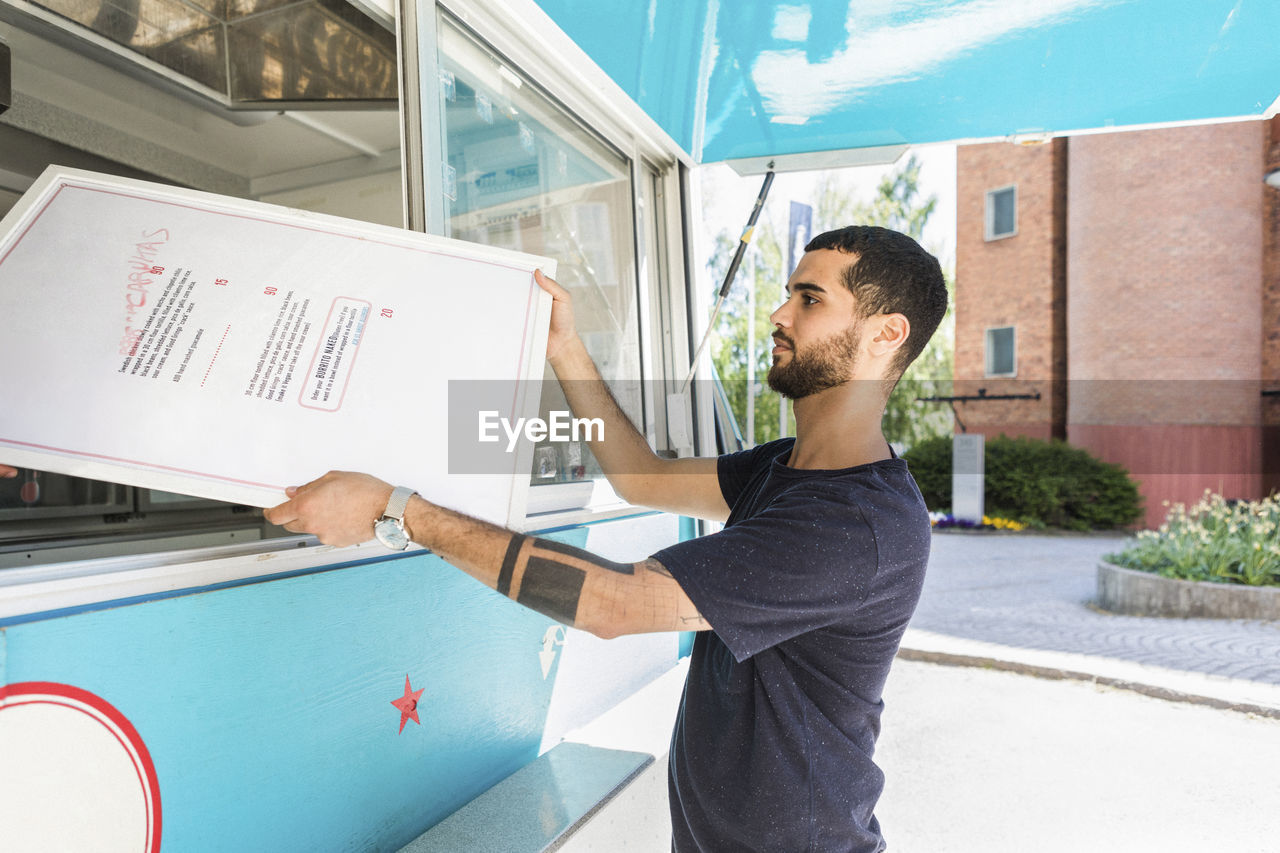 Side view of confident young male salesman holding menu placard at food truck