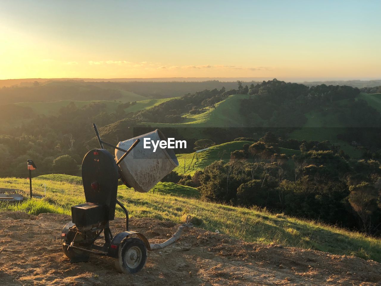 Machinery on hill against sky during sunset