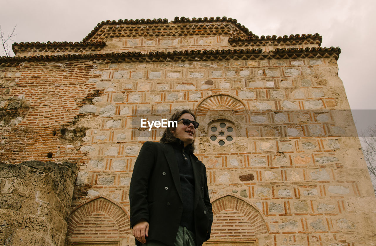 LOW ANGLE VIEW OF MAN STANDING AGAINST BUILDING