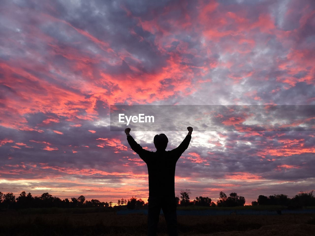 Silhouette man with arms raised standing against sky during sunset