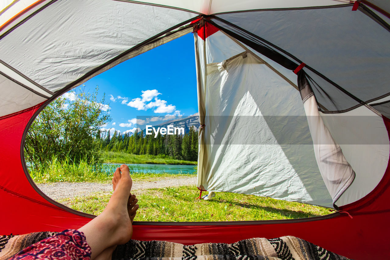 LOW SECTION OF PERSON RELAXING ON TENT AGAINST SKY