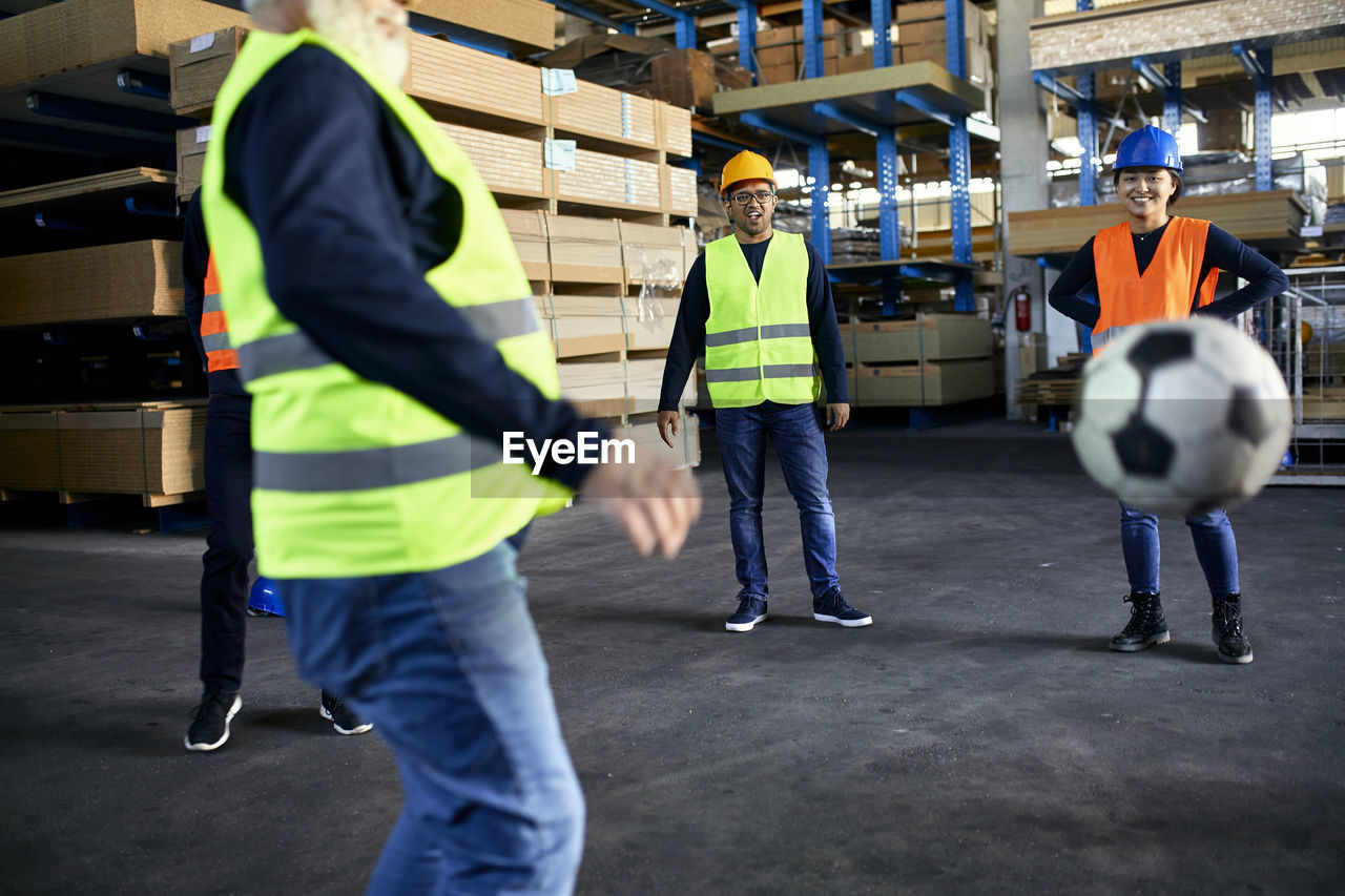 Workers playing football in factory warehouse