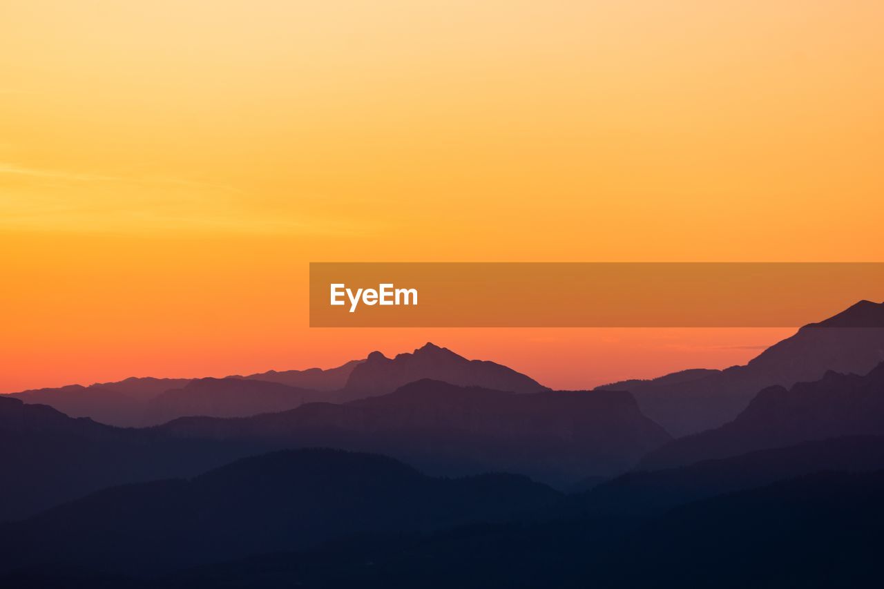 Scenic view of silhouette mountains against orange sky