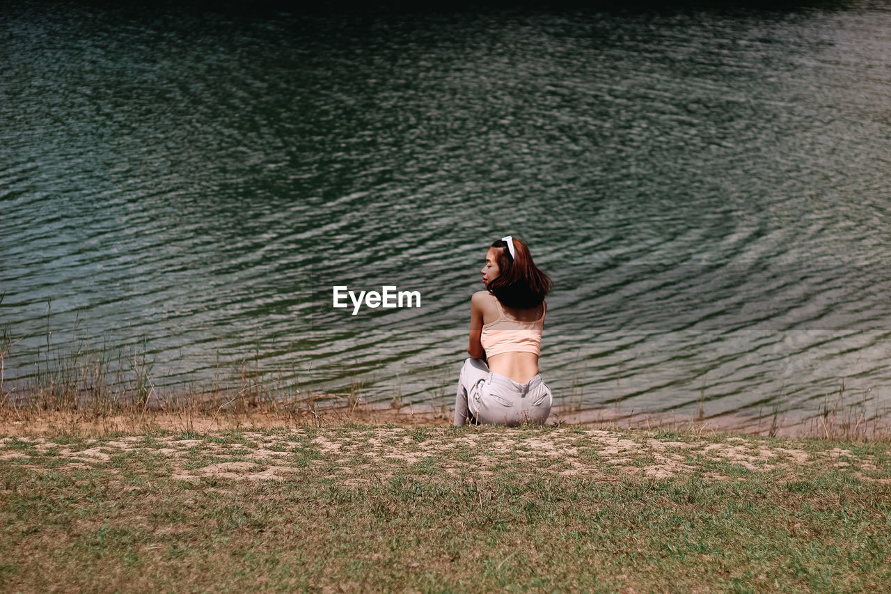 Rear view of woman sitting by lake