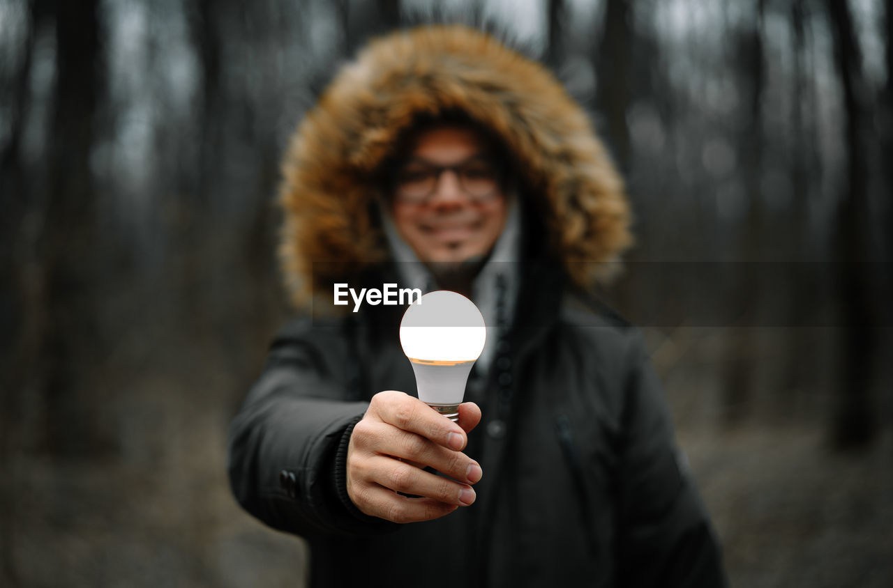 Smiling man holding illuminated light bulb in the forest