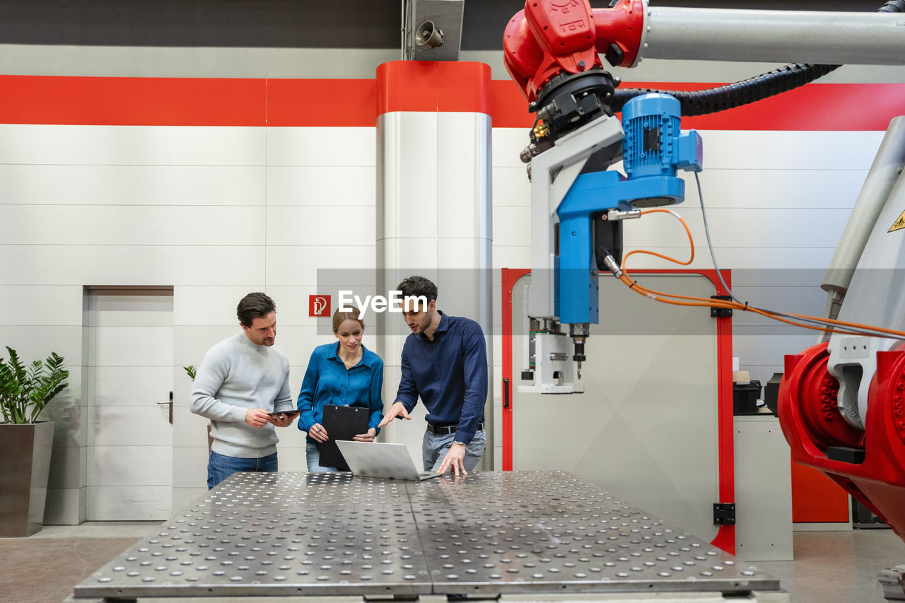 Colleagues working together over laptop in robot factory