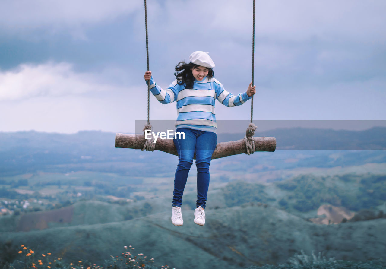 Smiling young woman swinging over landscape