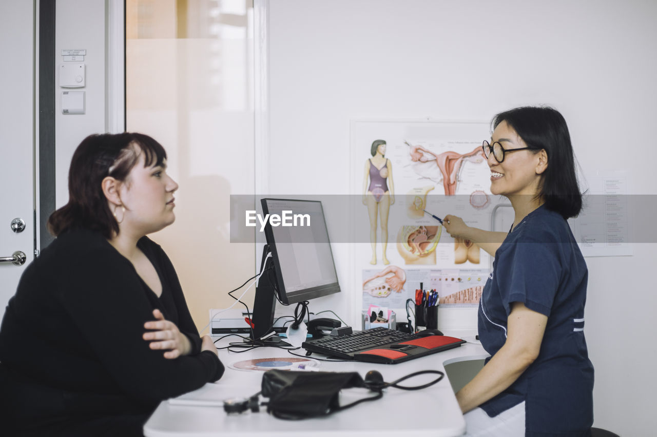 Smiling female doctor explaining to patient while pointing at organ chart in medical clinic