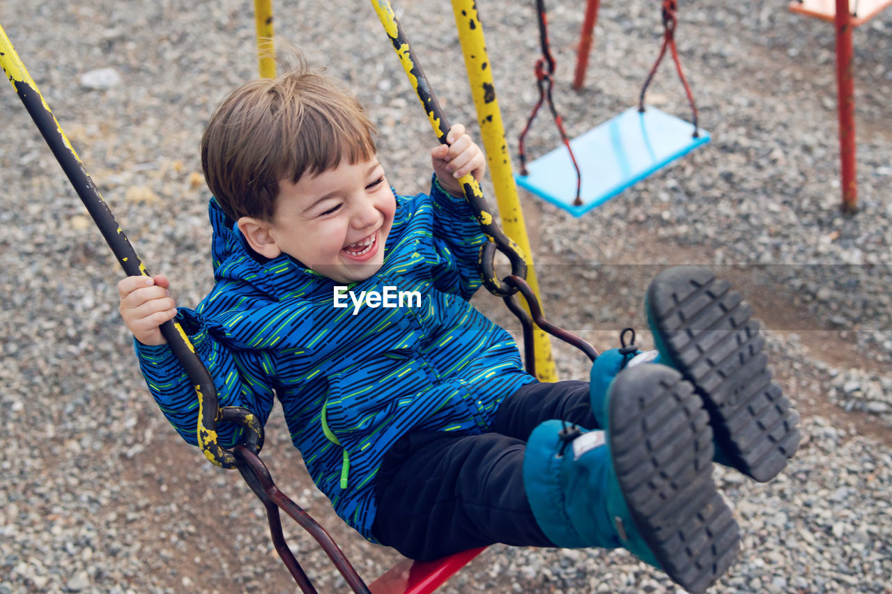 High angle view of cute boy playing on swing at playground