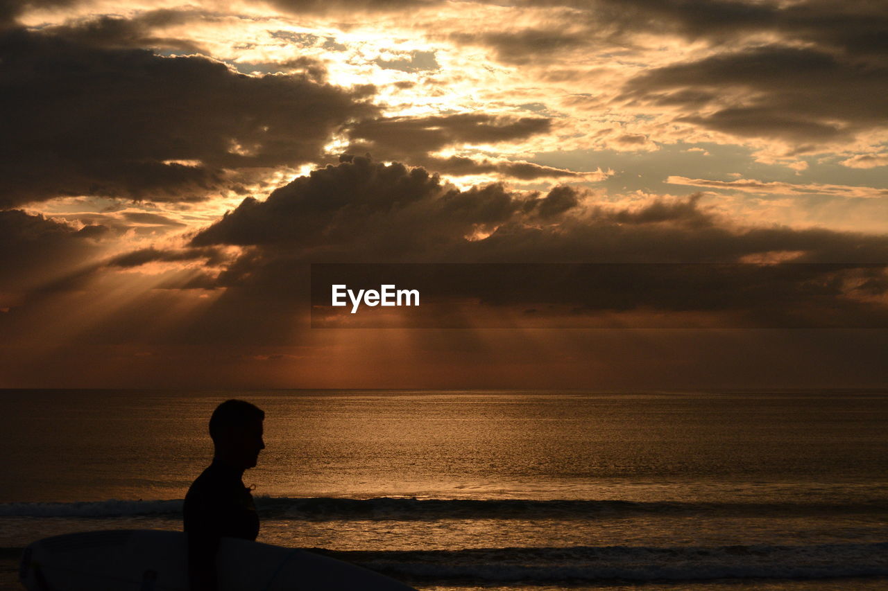 Silhouette man at beach against cloudy sky during sunset