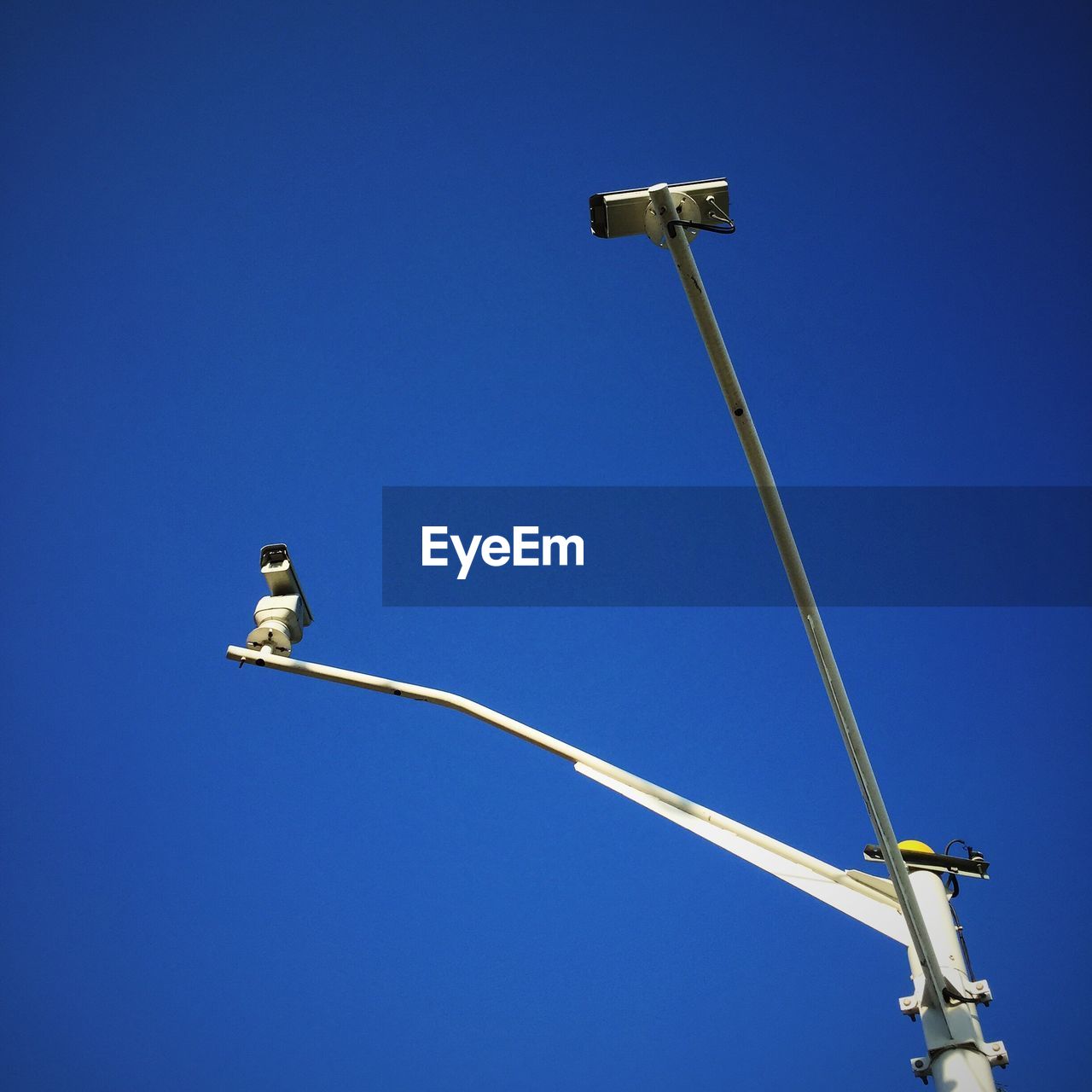 Low angle view of security cameras against clear blue sky