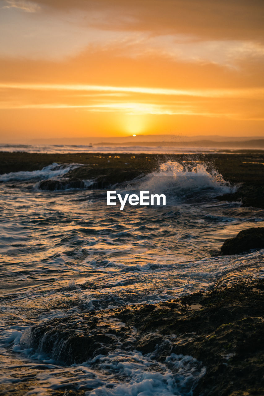 Image of the waves crashing on the rocks at sunset