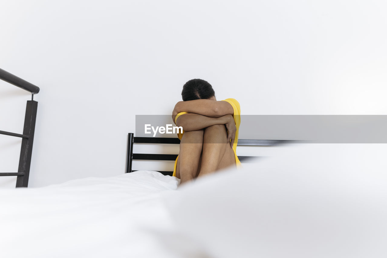 Sad young woman sitting on bed hugging knees