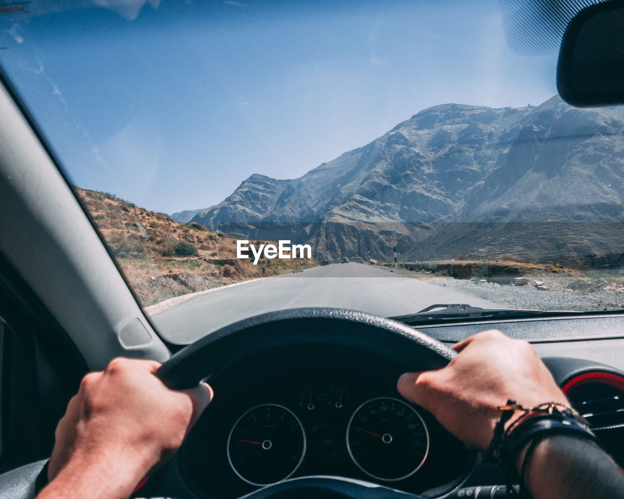 Cropped hands of man driving car on road against sky