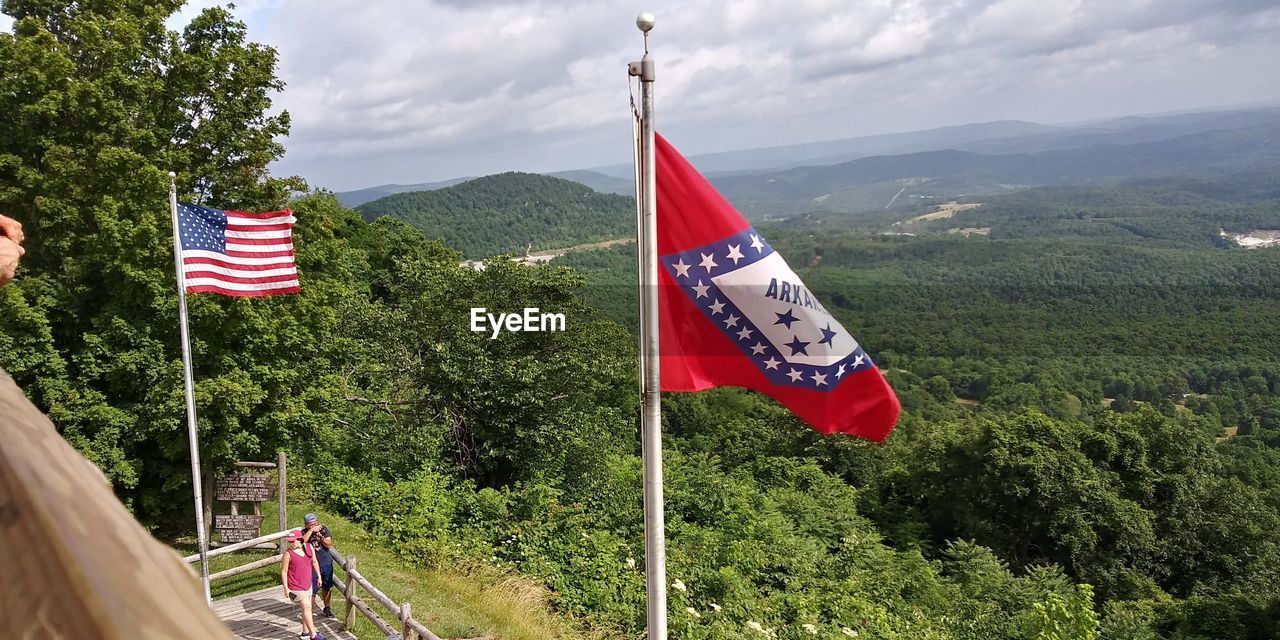 RED FLAG ON POLE AGAINST TREES AND MOUNTAINS