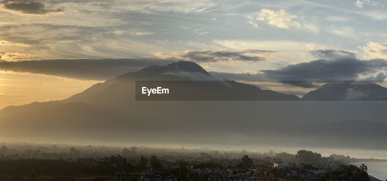 sky, environment, morning, mountain, landscape, cloud, dawn, sunrise, horizon, fog, scenics - nature, nature, beauty in nature, land, travel, travel destinations, sun, sunlight, mountain peak, mist, mountain range, architecture, no people, outdoors, tourism, city, tranquility, tree, sunbeam, twilight, forest, plant, cold temperature, dramatic sky, cloudscape, tranquil scene, winter, building, social issues, idyllic, trip, holiday, vacation, summer, atmospheric mood