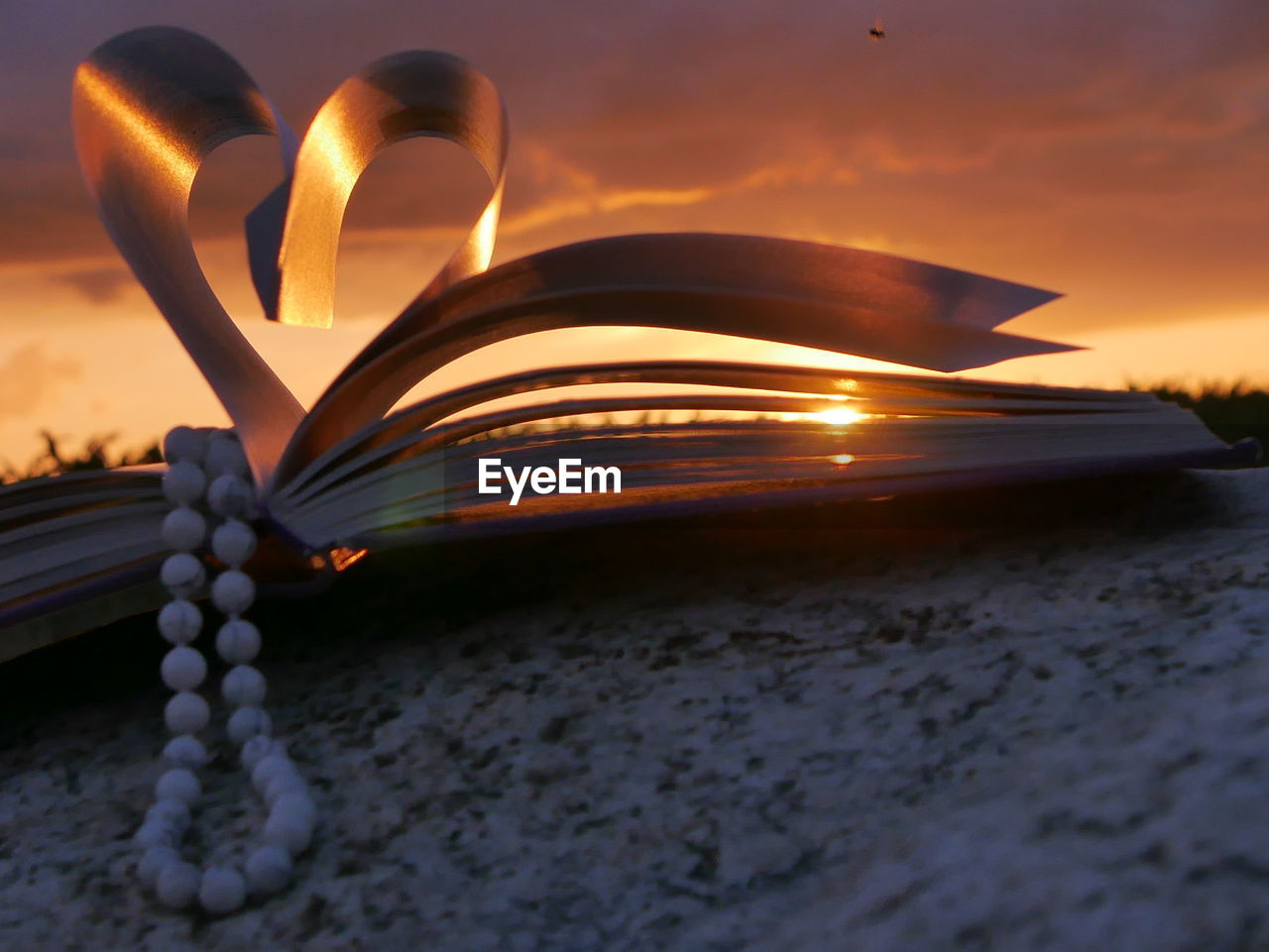 Bead necklace with heart shape folded pages of book during sunset