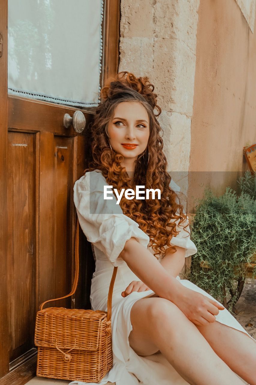 Smiling mid adult woman looking away while sitting against closed door