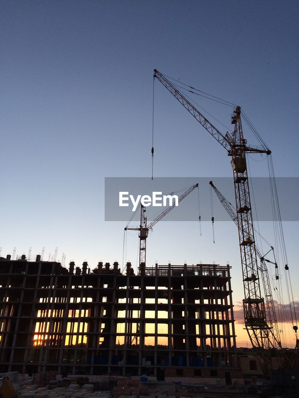 Low angle view of buildings and cranes at construction site against sky during sunset