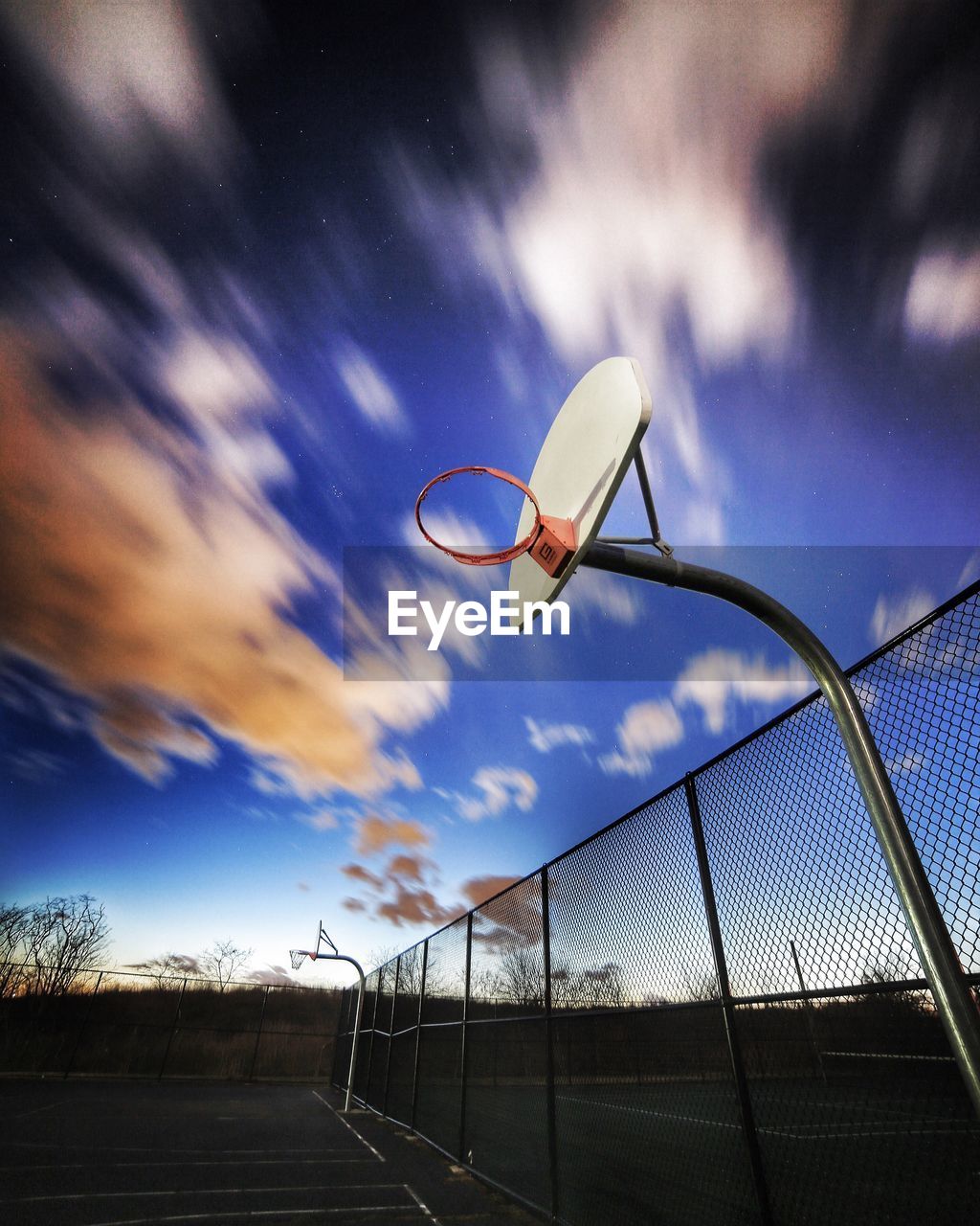 Low angle view of hoop in basketball court at sunset