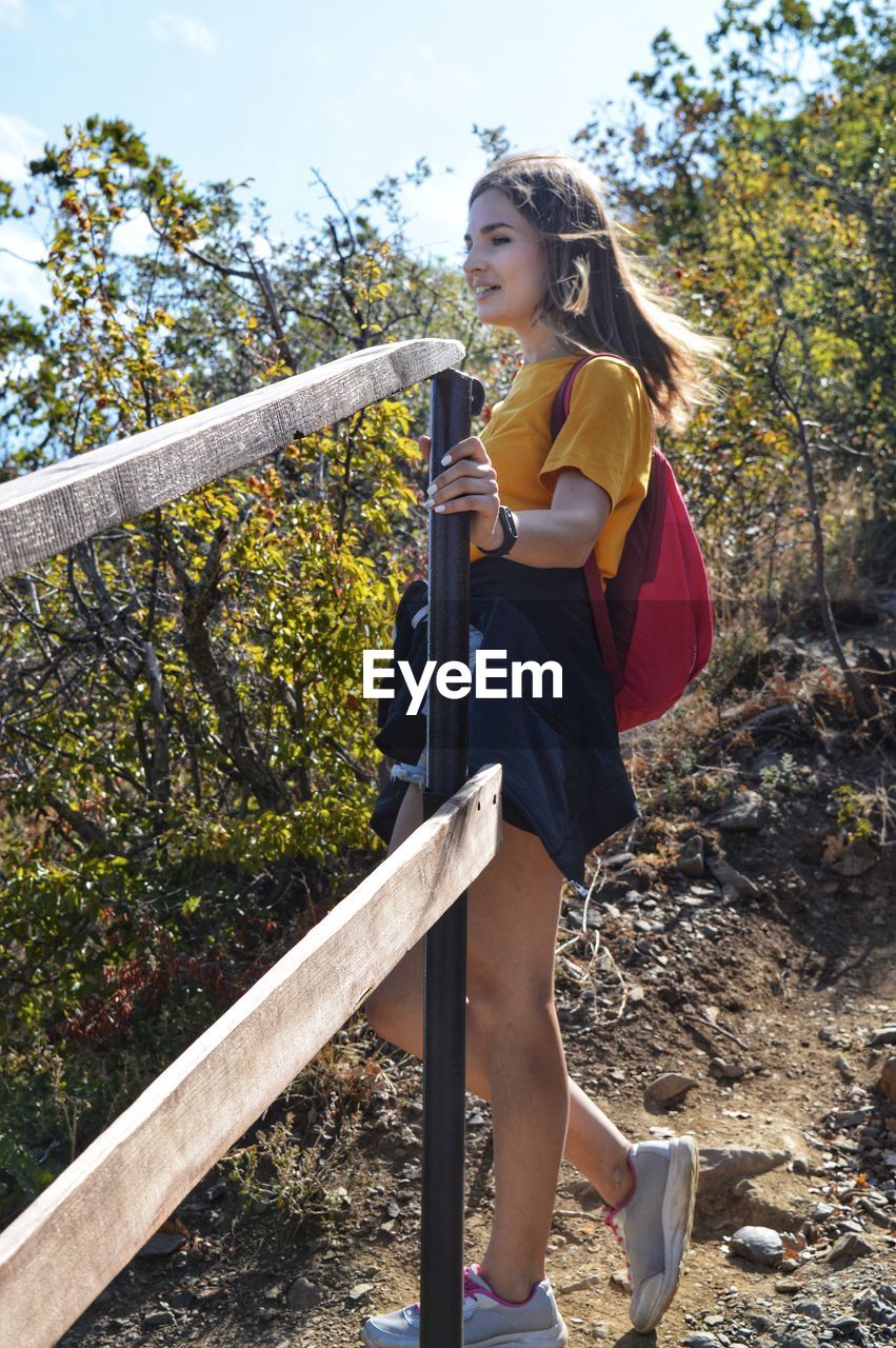 Young woman looking away while standing against trees