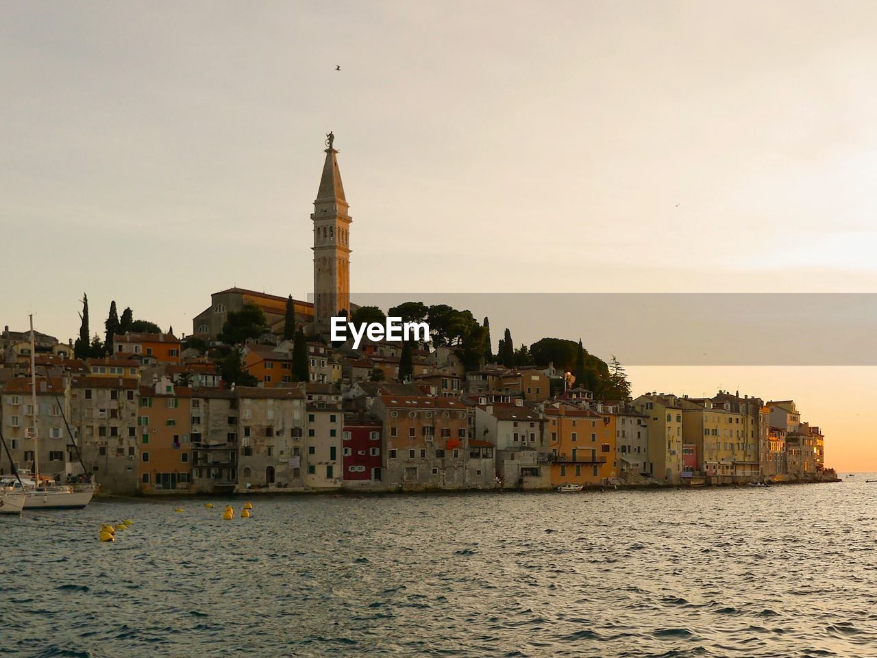 Buildings by sea against sky during sunset