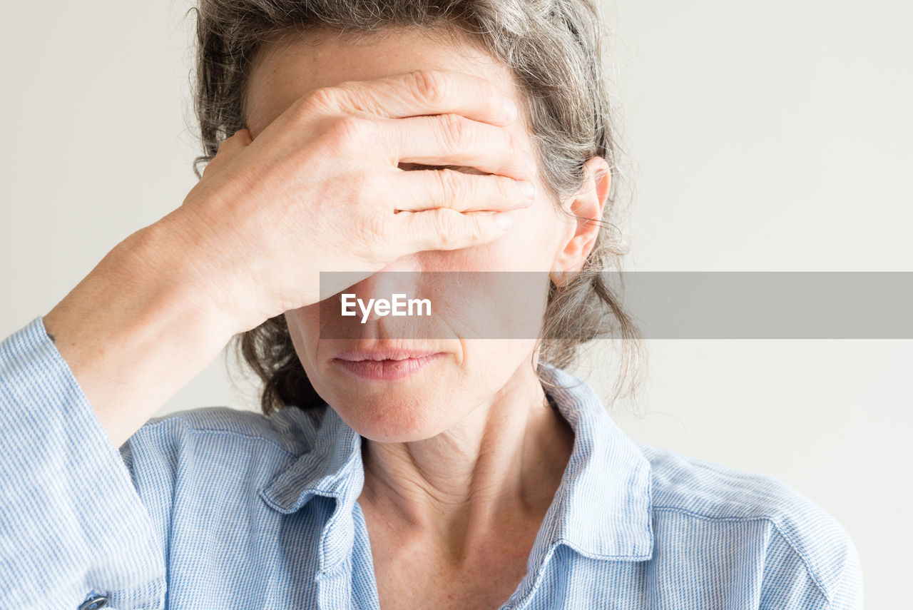 Close-up of woman covering eyes with hands against wall