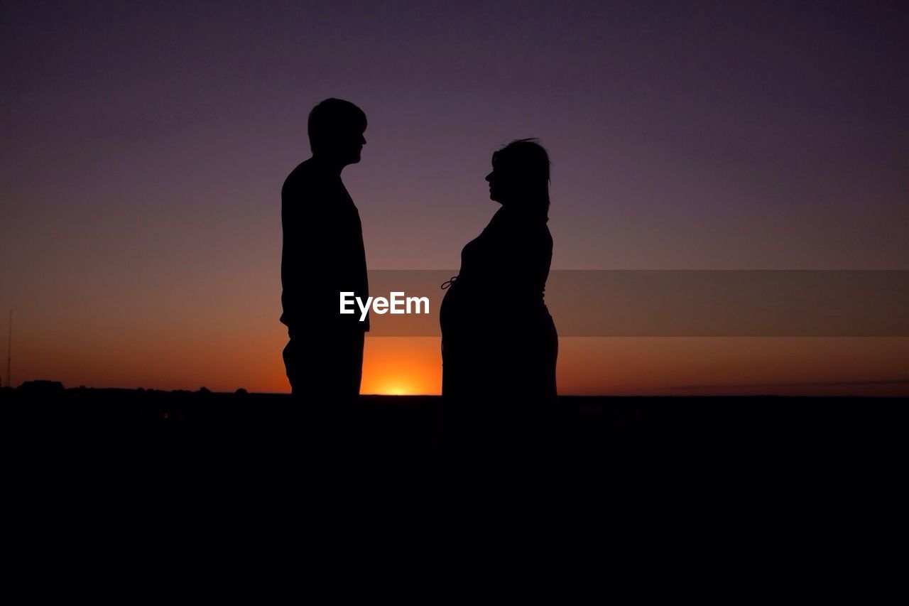 Side view of silhouette couple standing against sky during sunset