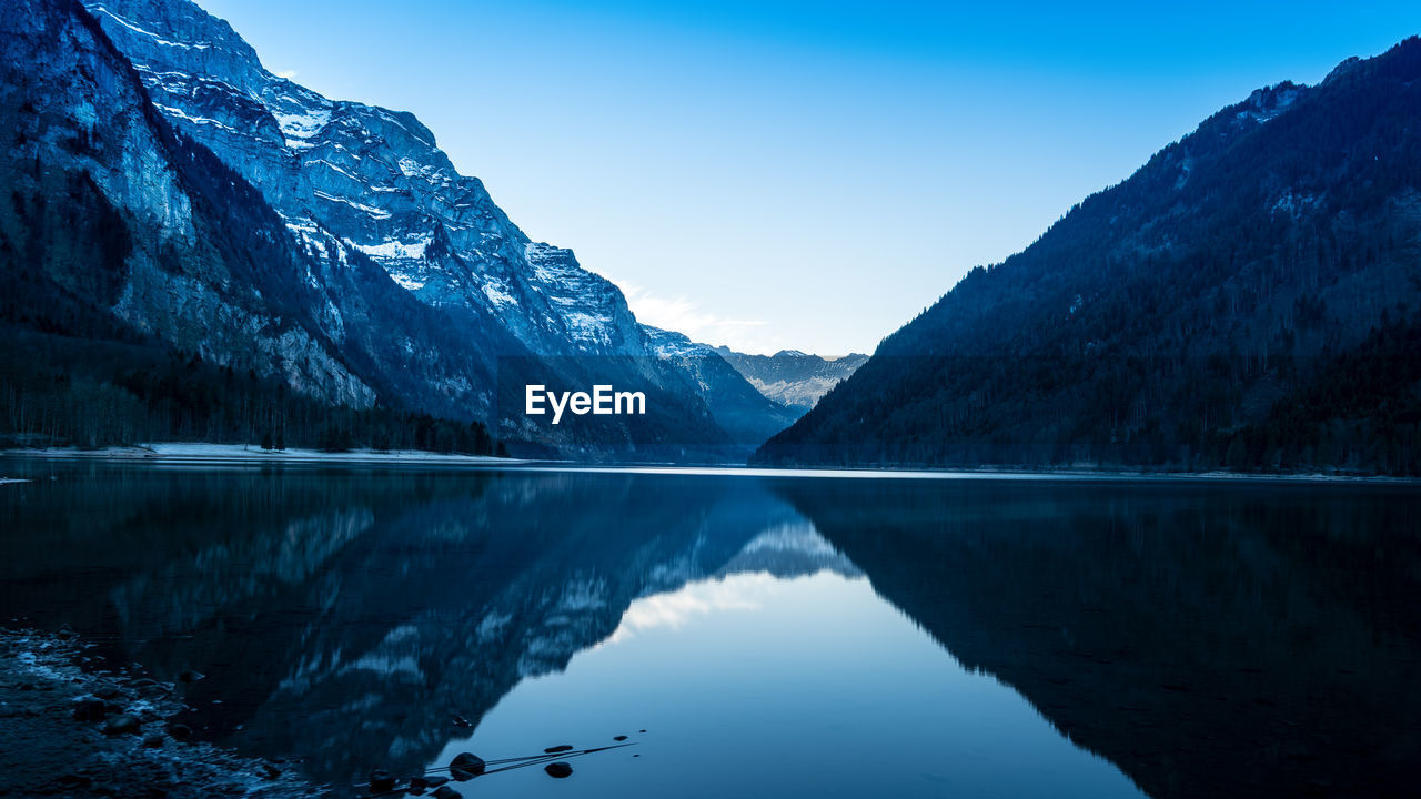 Scenic view of lake and mountains against clear blue sky