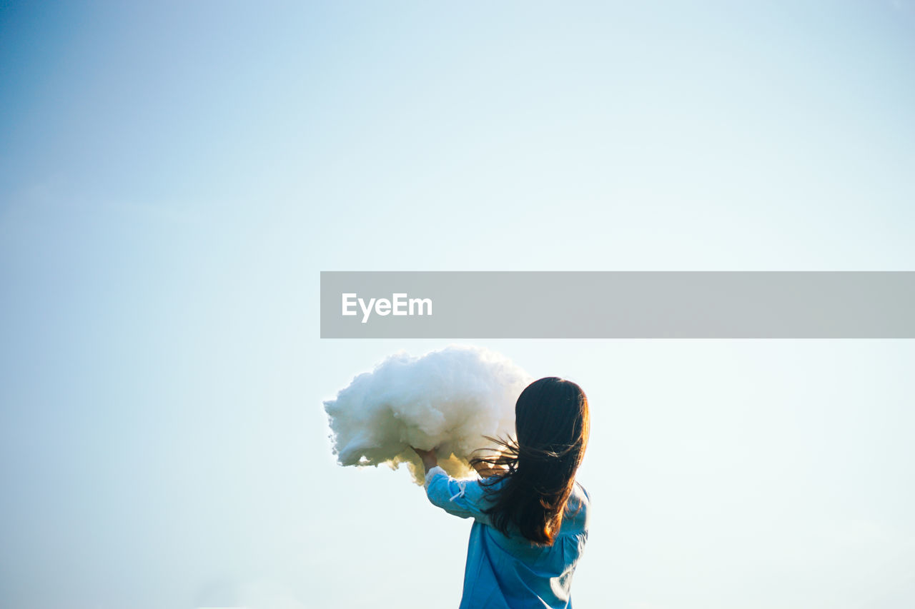 Girl holding up cloud against clear sky