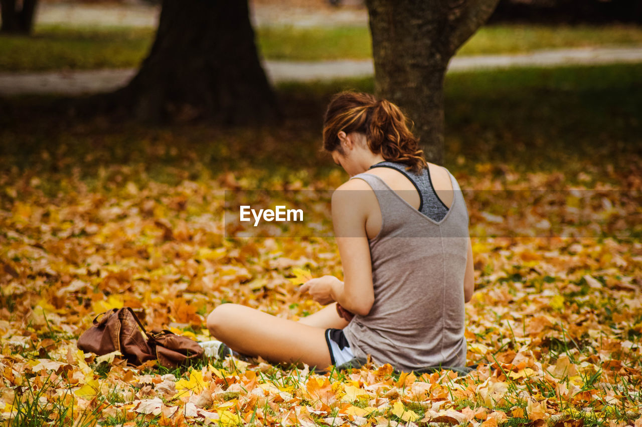 Rear view of woman sitting on fallen dry leaves at park during autumn