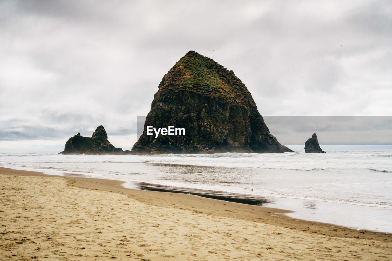 Scenic view of cannon beach against cloudy sky