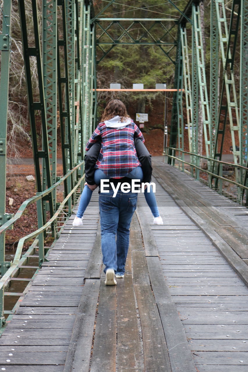 Rear view of boyfriend piggybacking girlfriend while walking on footbridge