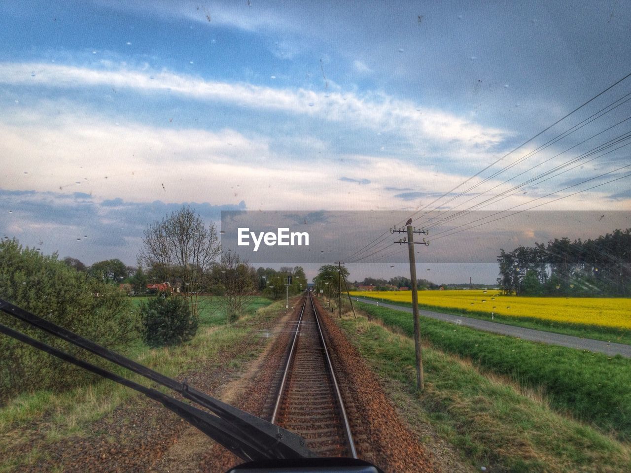 Railroad track on field against sky seen through train windshield