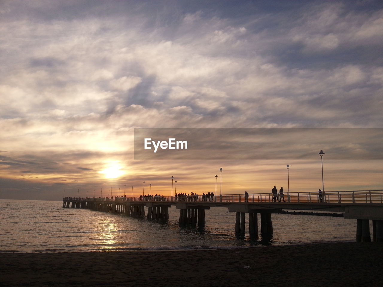 Pier on shore and sea against cloudy sky during sunset