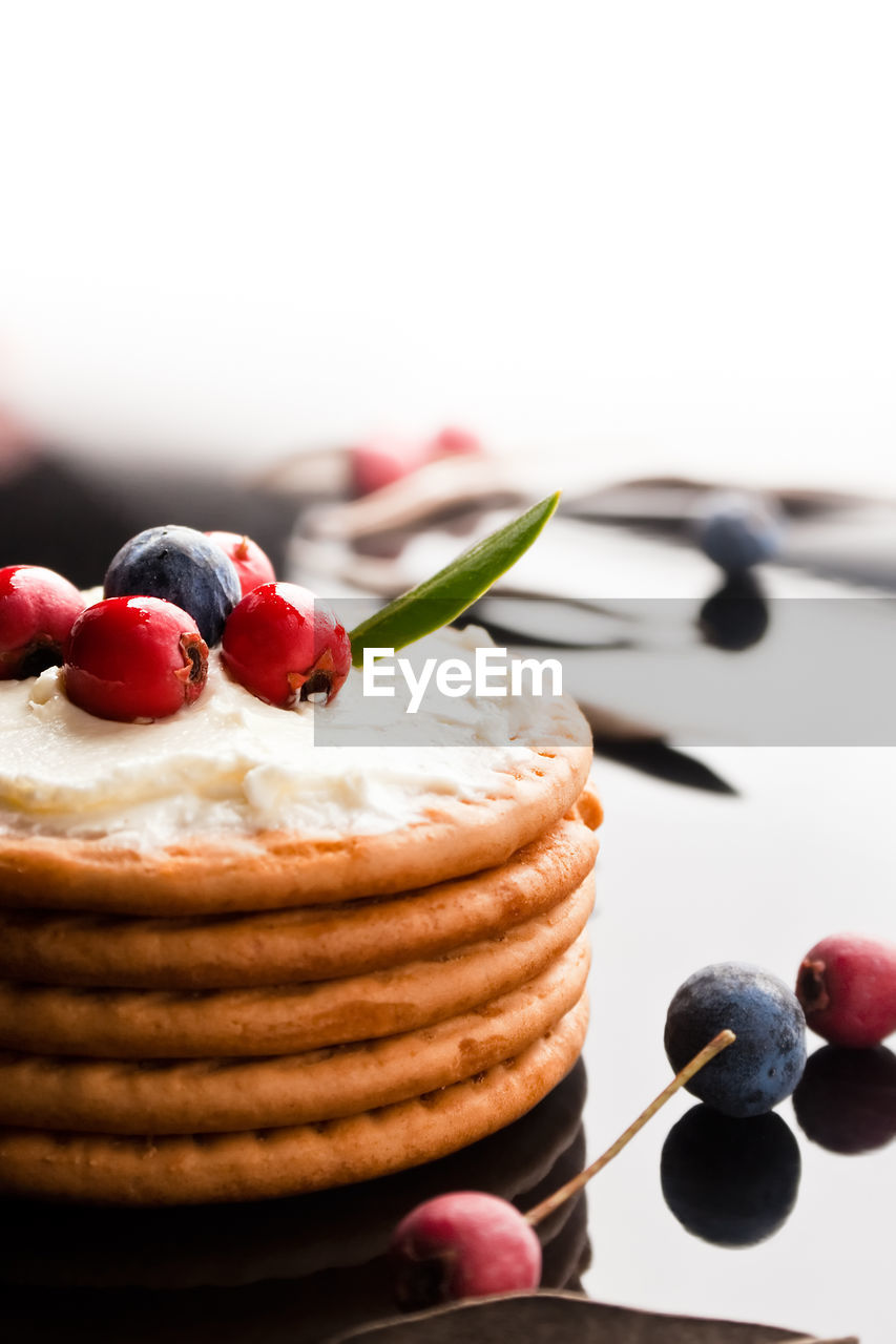 Cookies with cream cheese and blueberries in a dark plate surrounded with berries and dry leaves