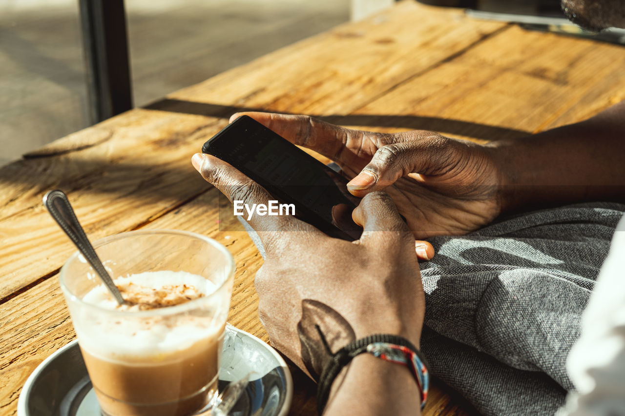 Cropped hands of man using phone while sitting at table in cafe