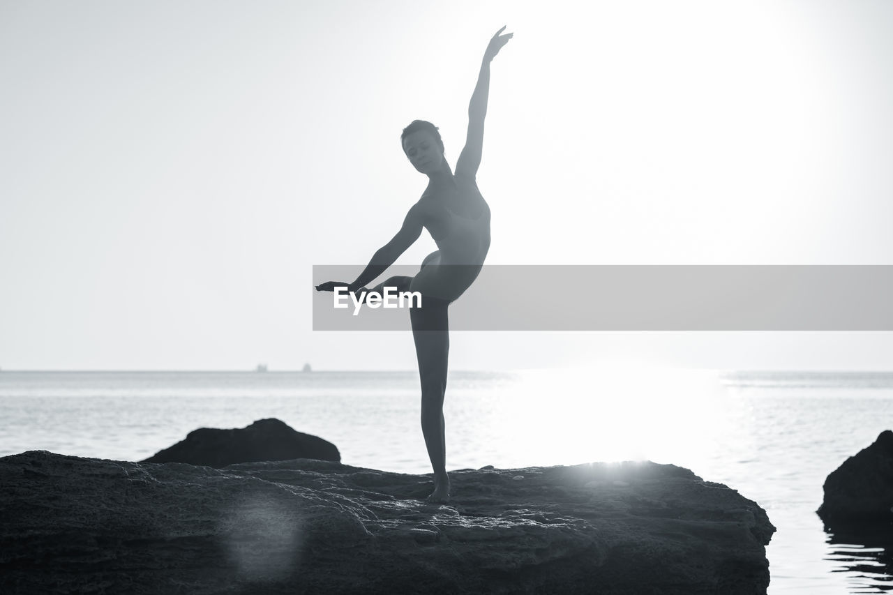 Woman dancing on rock against sea during sunny day