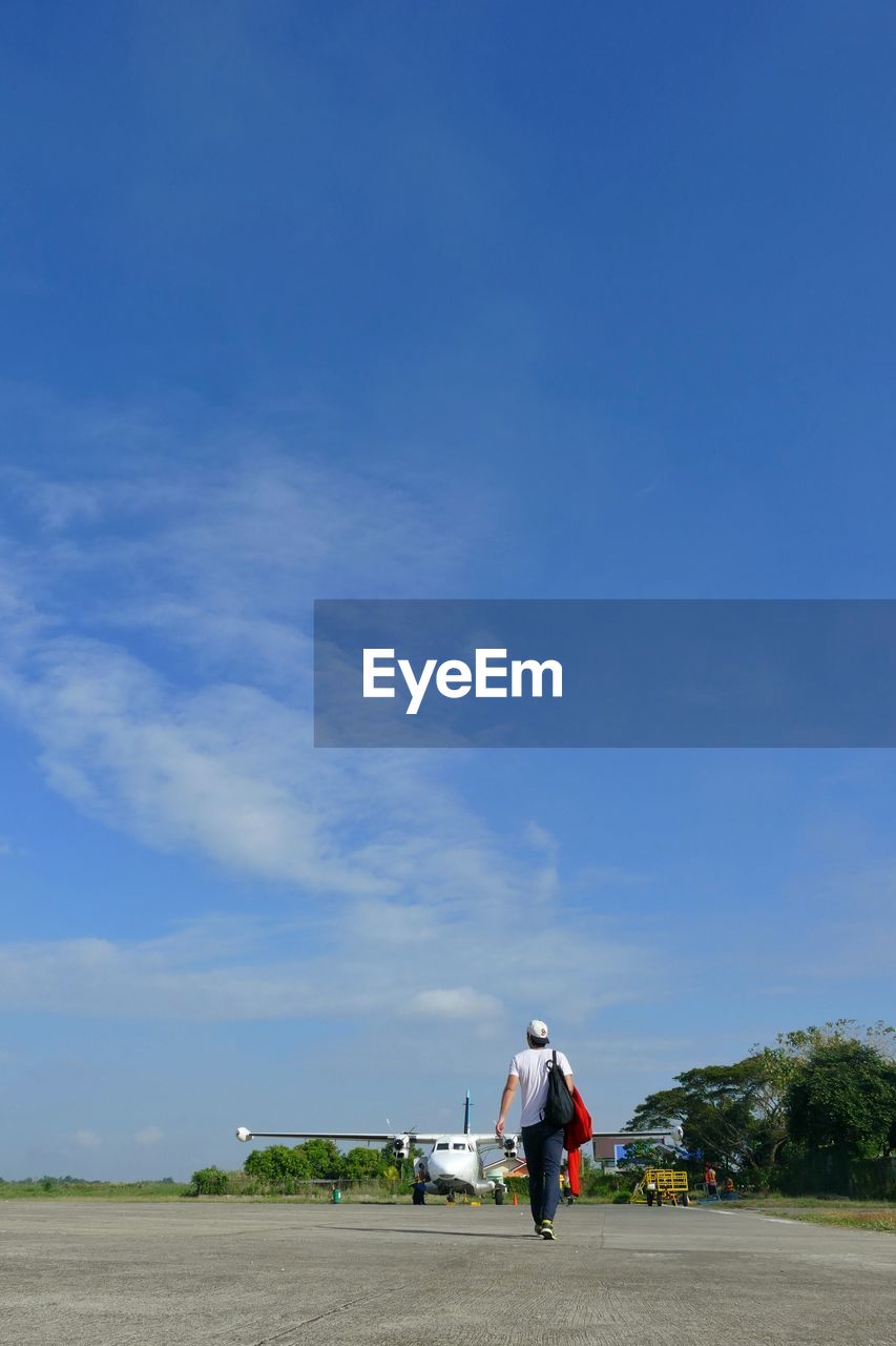 Rear view of man walking on runway against sky