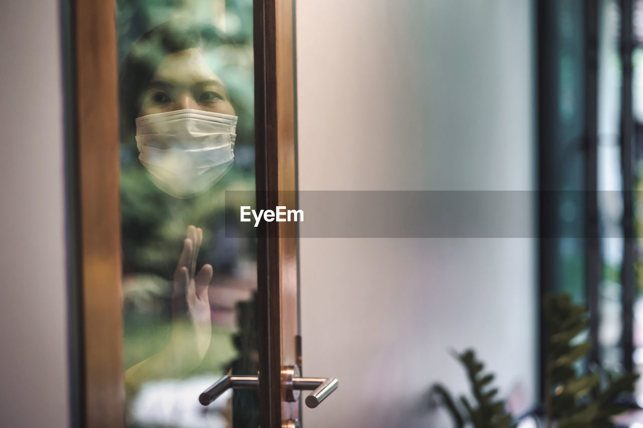 Woman wearing mask seen through glass door