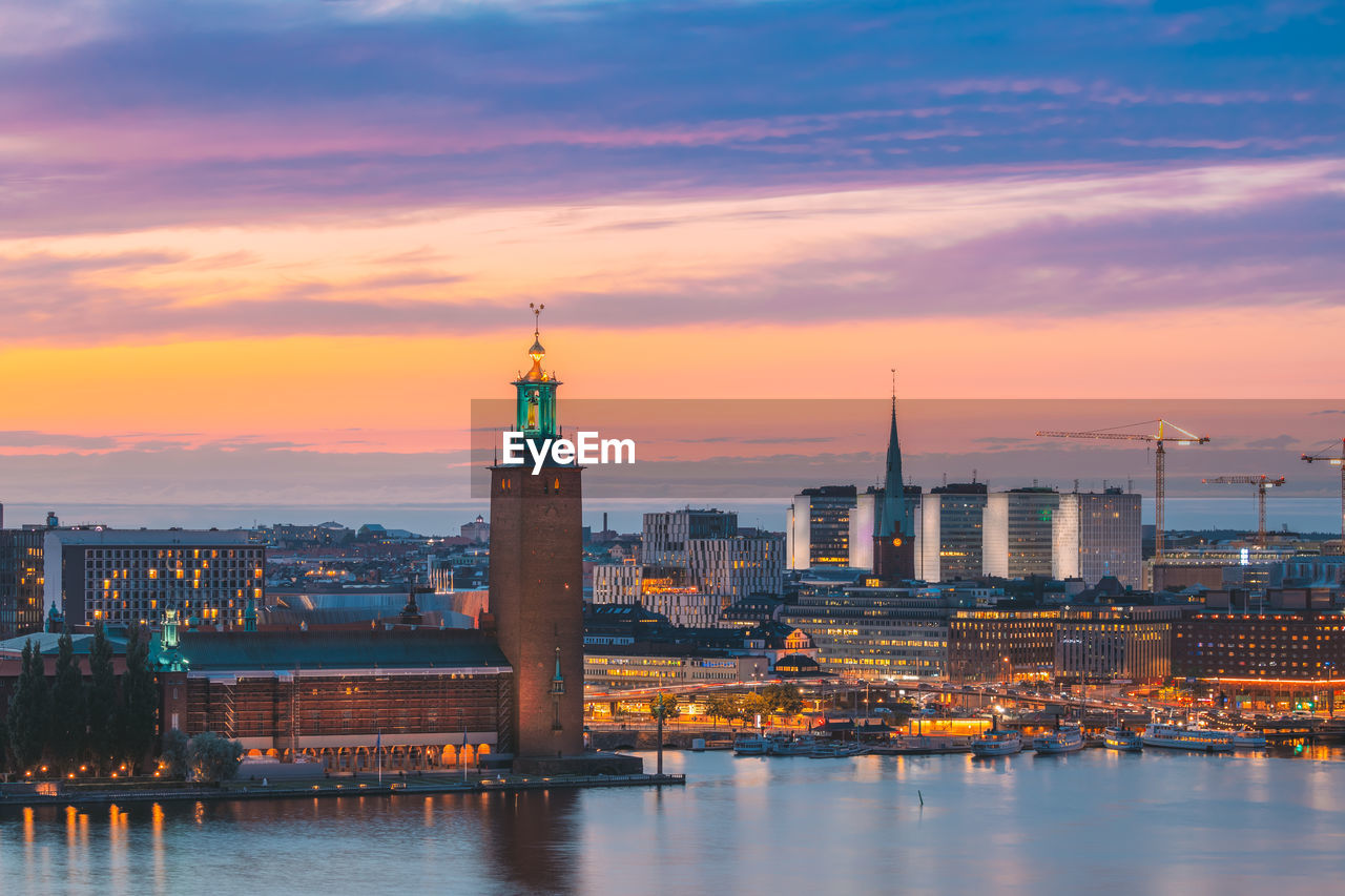 buildings by river against cloudy sky during sunset