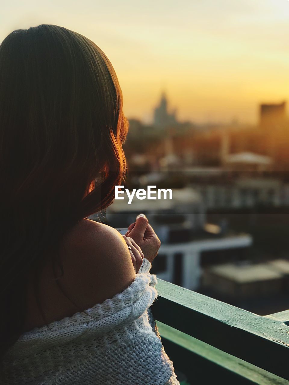 REAR VIEW OF WOMAN HOLDING RAILING AGAINST SKY